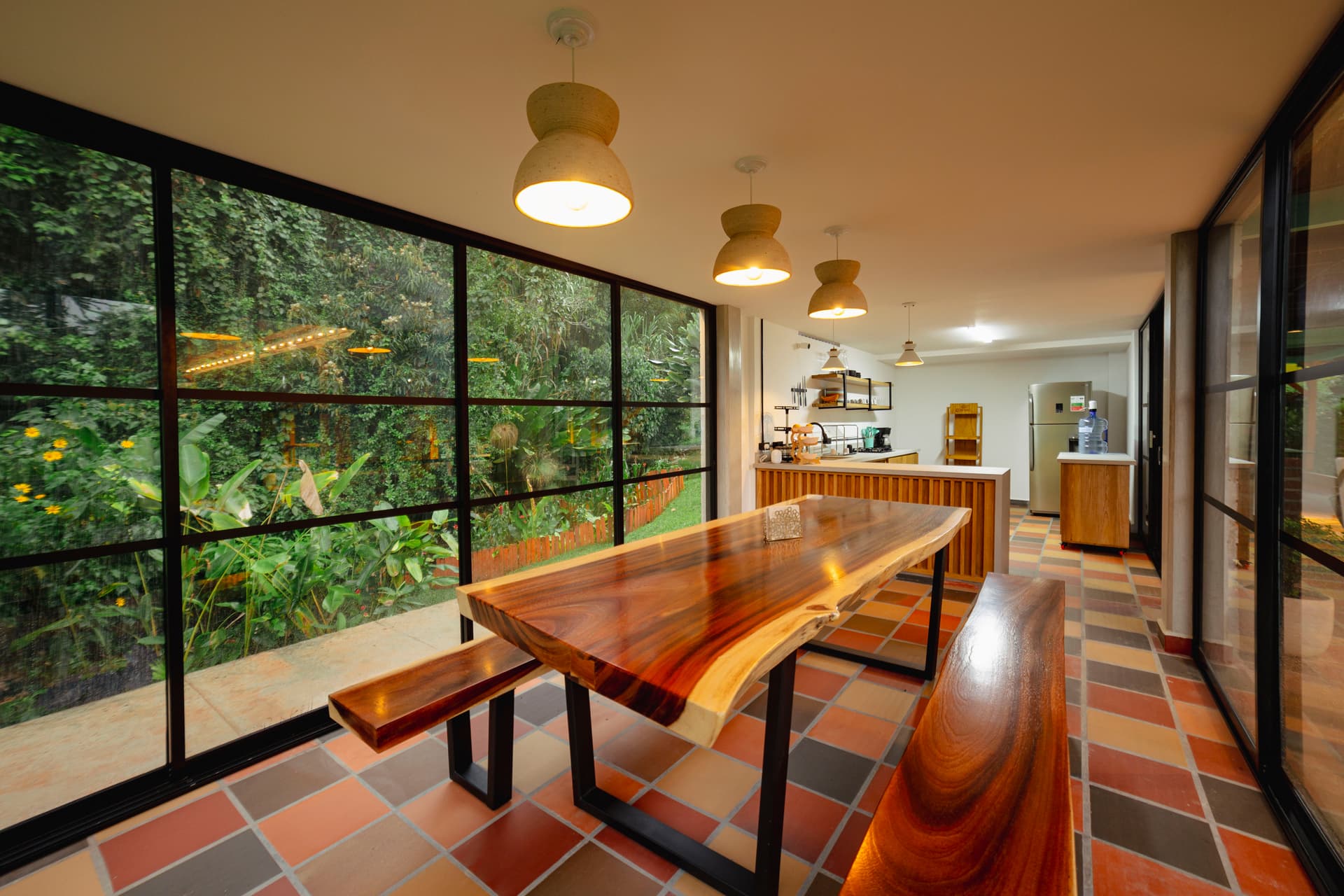 Long live-edge wooden dining table and benches inside the black-framed glazed kitchen wing